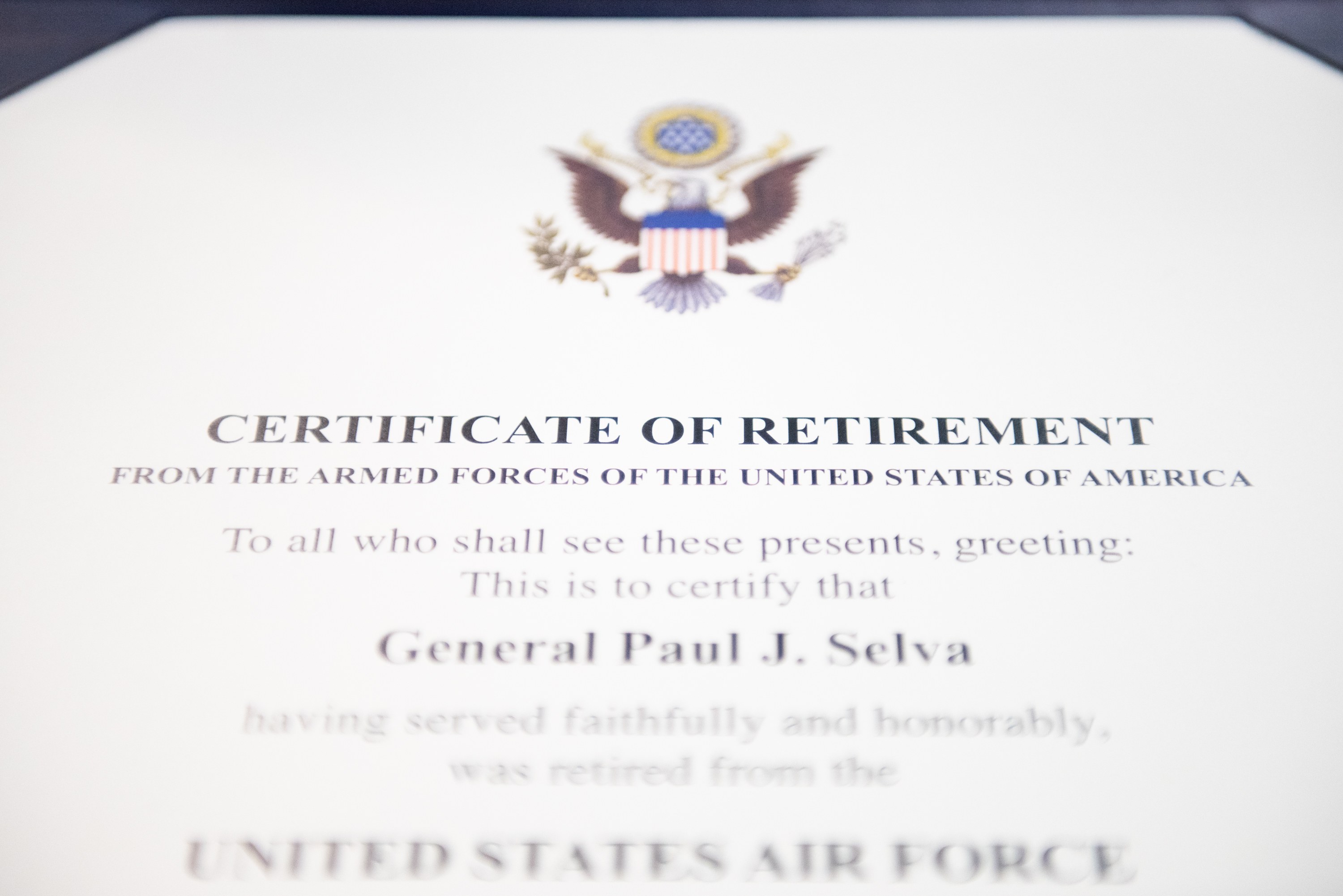 Rahmenurkunde zur Verabschiedung von der United States Air Force mit blauem Rand, die ein schwarzes Textfeld und ein zentrales Schild-Logo mit einem Stern, einem Lorbeerkranz und einer 'Verabschiedung'-Banderole zeigt.