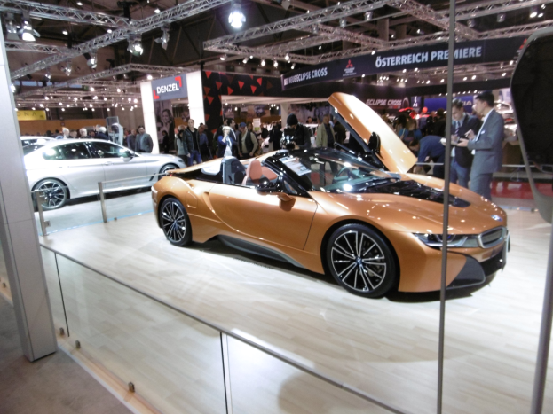 Ein stylischer schwarzer BMW i8 Roadster mit Chromakzenten auf der Frankfurt Motor Show umgeben von formell gekleideten Gästen.
