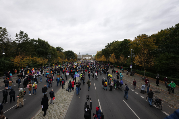 Eine große Gruppe von Menschen, die eine straße mit Bäumen und Laternen entlangmarschieren, mit Kameras in der Hand, vor einem Gebäude unter einem klaren Himmel.
