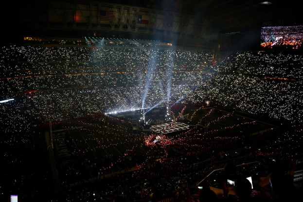 Große Menschenmenge in einem hell erleuchteten Stadion bei Nacht, mit einem Bildschirm auf der rechten Seite, der die Ergebnisse der Super Bowl XLVII-Halbtzeitshow anzeigt.