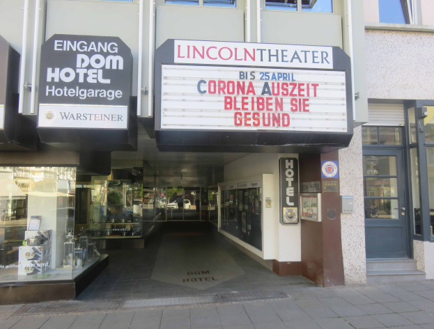 Das Lincoln Theater in Berlin, Deutschland - ein Gebäude mit Glasfenstern und -türen sowie einer Tafel mit Text, die verschiedene Objekte im Inneren zeigt und so einen Eindruck von einer pulsierenden Stadtlandschaft vermittelt.