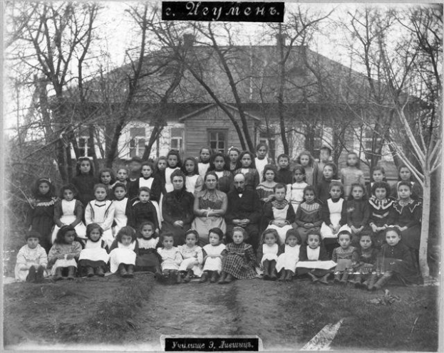 Schwarzes-Weiß-Foto von Kindern, die vor einem Gebäude mit Fenstern posieren, umgeben von Bäumen und einem klaren Himmel, mit Text unten: "Jugoslawien, die erste Schule der Welt".