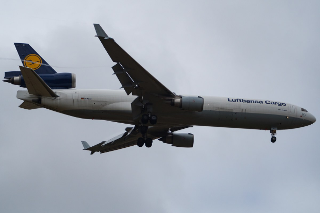 Ein Lufthansa Cargo Boeing 777-300ER im Flug, mit ausgebreiteten Flügeln und laufenden Triebwerken, mit "Lufthansa Cargo"-Text auf dem Rumpf gegen einen bewölkten Himmel.