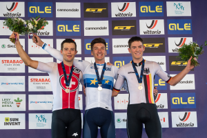 Drei Männer stehen auf einem Podium, jeder mit einer Medaille und einem Blumenstrauß in der Hand, vor einem "Giro d'Italia"-Schild im Hintergrund.