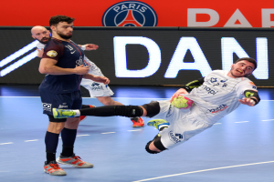 Eine Gruppe von Männern spielt Handball auf einem Platz, einer hält einen Ball, mit einem Hintergrund-Plakat der Paris Saint-Germain Futsal-Mannschaft.