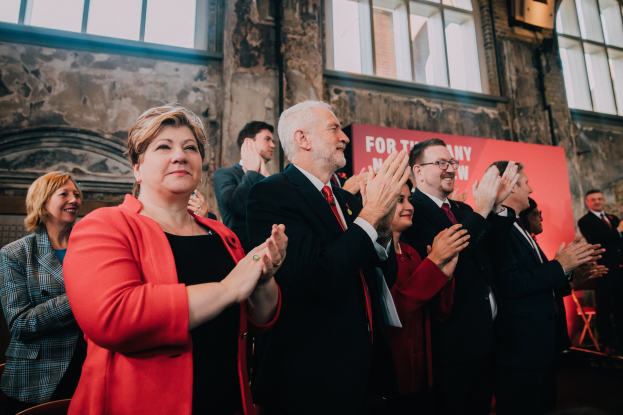 Menschen klatschen feiernd vor einer Menge mit einem Wahlsieg-Plakat im Hintergrund.
