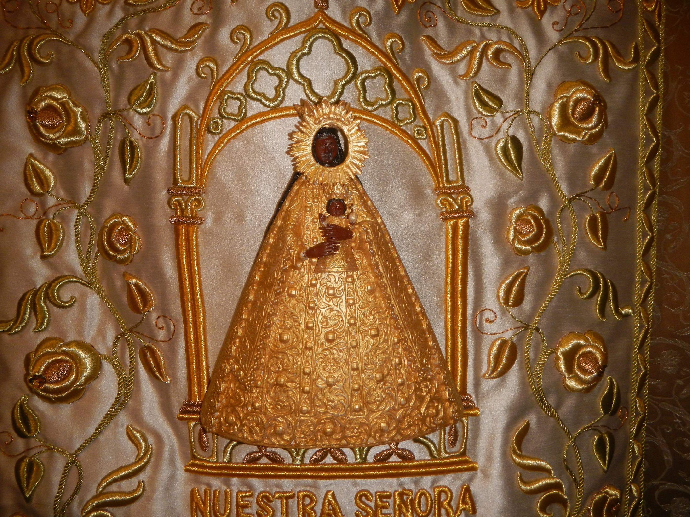 Goldene Stickerei mit einer seren Frau in einem hochgeschlossenen, langärmligen Kleid mit einem Dutt, umgeben von detaillierten Texten und prächtigen goldenen Designs.