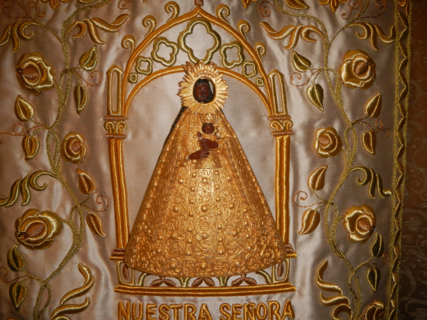 Goldene Stickerei mit einer seren Frau in einem hochgeschlossenen, langärmligen Kleid mit einem Dutt, umgeben von detaillierten Texten und prächtigen goldenen Designs.