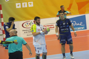 Eine Gruppe von Männern steht auf einem Futsal-Platz, einer hält einen Ball, links ist ein Tor und im Hintergrund Banner zu sehen.