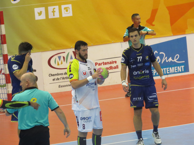 Eine Gruppe von Männern steht auf einem Futsal-Platz, einer hält einen Ball, links ist ein Tor und im Hintergrund Banner zu sehen.