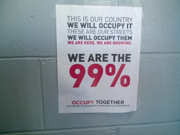 Schwarzes Plakat an einer Wand mit fett gedrucktem Text "Occupy Wall Street" und "Wir sind die 99%".