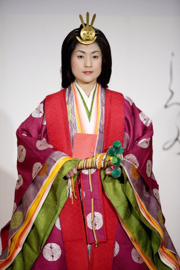 Eine Frau in einem traditionellen japanischen Kimono steht selbstbewusst auf einem Laufsteg und trägt ein leuchtend rotes und grünes Kleid mit aufwändigen Mustern und ihrem Haar zu einem ordentlichen Knoten gebunden.