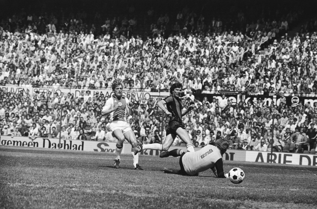 Schwarzes und weißes Foto von Männern, die auf einem Feld Füßball spielen, mit Zuschauern im Hintergrund und einer Tafel mit der Aufschrift "Bundesliga 1978-79 Ajax 1-1 Hannover 96."