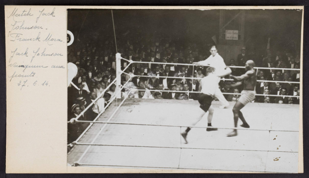Schwarzes und weißes Foto von zwei Boxern in einem Ring, beschriftet mit 'Jack Johnson vs Frank Morgan', mit Zuschauern dahinter und einer Wand im Hintergrund.