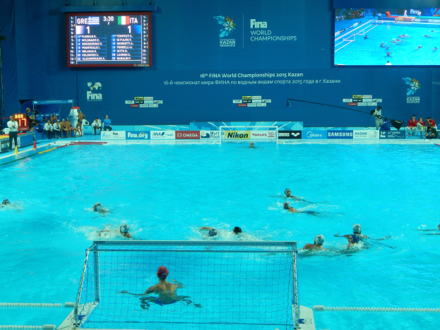 Wasserballspieler bei den FINA-Weltmeisterschaften 2016 in Kazan im Pool gegeneinander antretend, mit Zuschauern links und einer Anzeigetafel im Hintergrund.