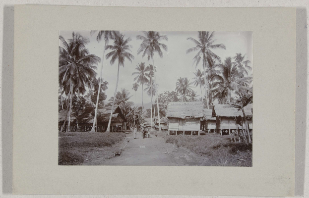 Schwarzes und weißes gerahmtes Foto eines Dorfes mit Hütten, Menschen und Palmen.