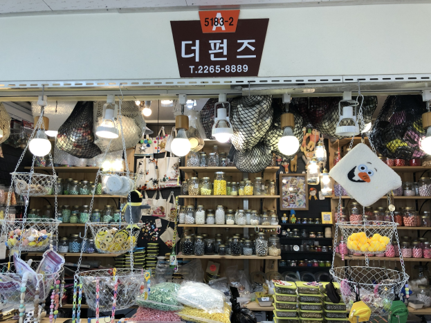 Ein unordentlicher Laden in Seoul, der verschiedene Gegenstände wie Körbe, Lampen, Flaschen und Spielzeuge auf Regalen ausstellt, mit einer Tafel oben, die anzeigt, dass es der beste koreanische Shop ist.