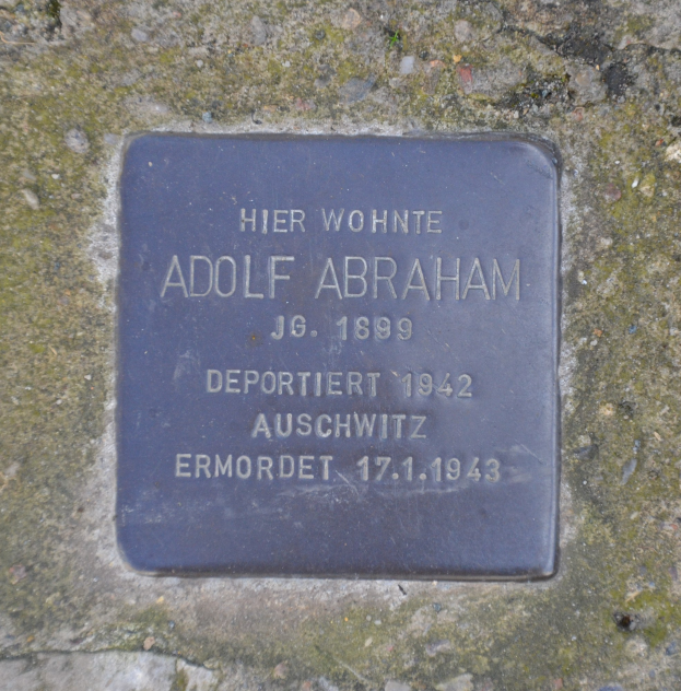 Rechteckige Plakette an einer Steinwand mit der Inschrift "Adolf Abraham".