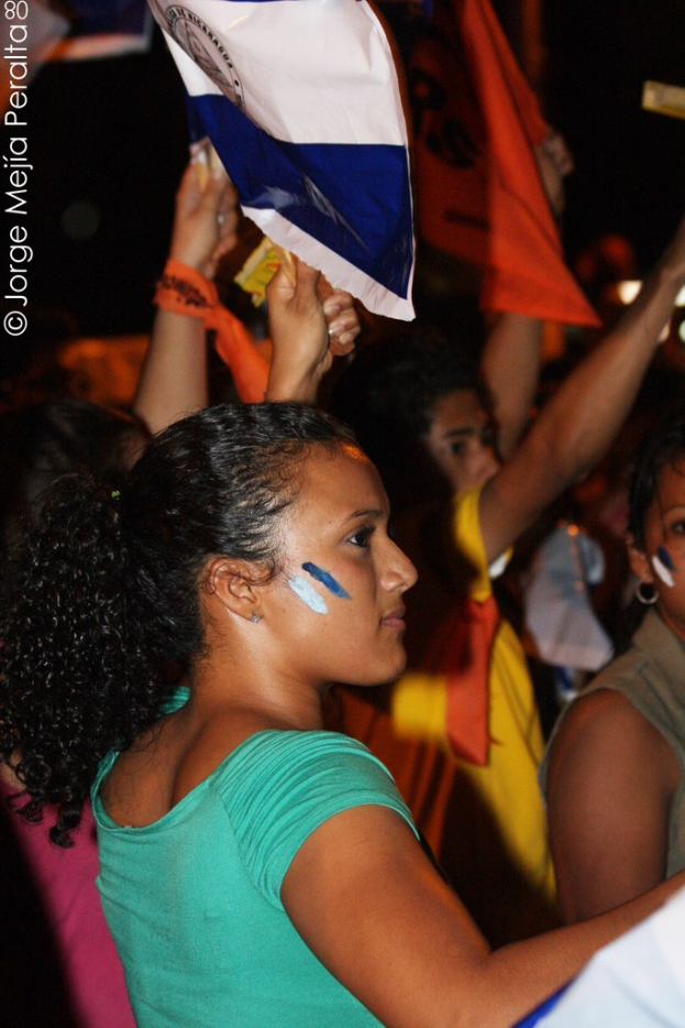 Frauen in grünen T-Shirts bei einer Demonstration, die weiße Schilder halten, mit anderen Mädchen im Hintergrund.