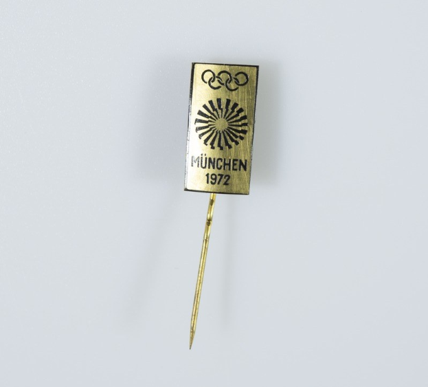 Goldnadel mit «München 1972 Olympische Spiele» Text auf weißem Hintergrund.