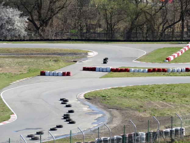 Rennstrecke voller Reifen, gesäumt von Gras und Maschendrahtzaun, mit Bäumen im scenischen Hintergrund.