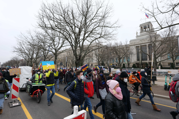 Eine große Gruppe von Menschen nimmt an einer Protestdemo in Washington, D.C. am 21. Januar 2020 teil und marschiert die Straße entlang, wobei einige Schilder und Plakate halten und andere Fahrräder fahren, mit Bäumen und einem klaren blauen Himmel im Hintergrund.