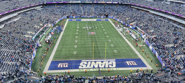 Ein volles Fußballstadion mit Spielern auf dem Feld, Torpfosten und Zuschauern in Sitzplätzen unter einer lebendigen Atmosphäre.