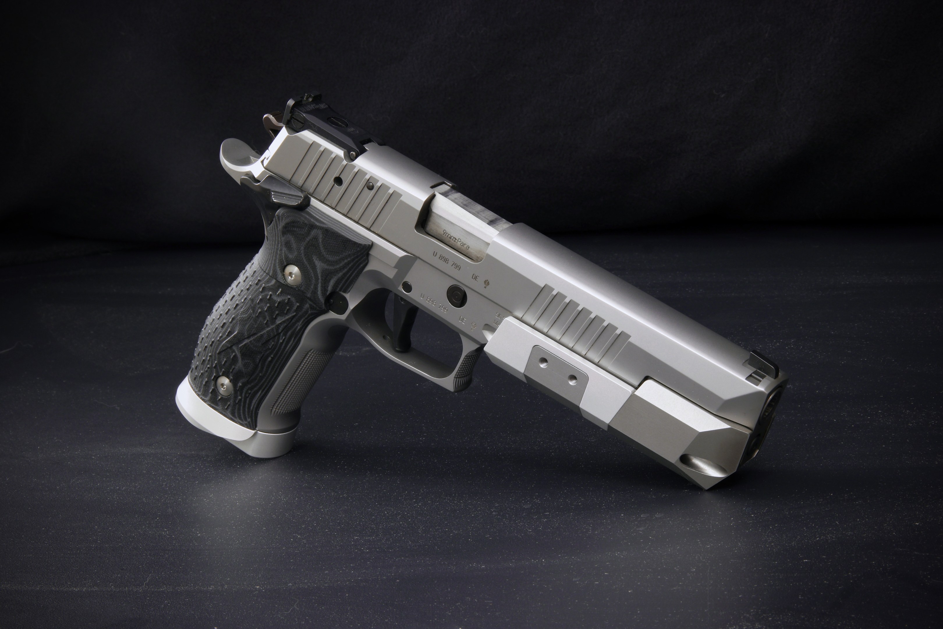 Eine Sig Sauer P226 X-Five 9mm Pistole auf einer schwarzen Oberfläche vor einem schwarzen Hintergrund.