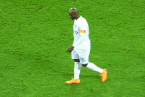 Ein Füßtballer in weißem T-Shirt, weißen Shorts und orangenen Schuhen läuft über ein grünes Feld.