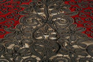 Nahaufnahme eines roten Kleids mit schwarzer Spitzenüberlagerung, das detaillierte Spitzenmuster auf dem roten Stoff zeigt.