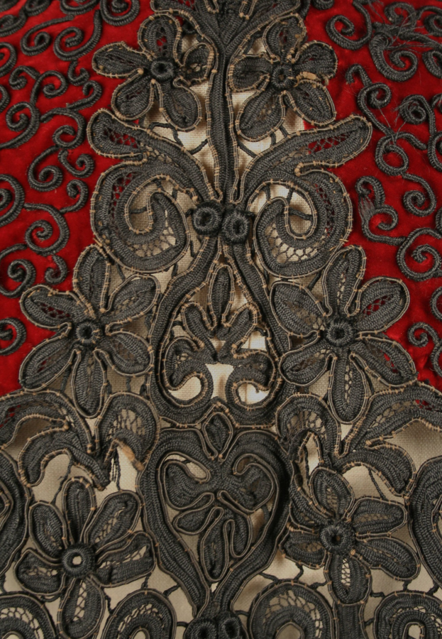 Nahaufnahme eines roten Kleids mit schwarzer Spitzenüberlagerung, das detaillierte Spitzenmuster auf dem roten Stoff zeigt.
