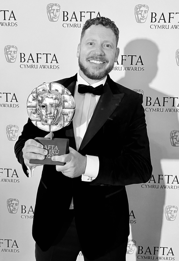 Ein Mann im Smoking, der eine BAFTA-Trophäe hält und lächelt, mit einer 'BAFTA Awards 2018'-Rückwand.