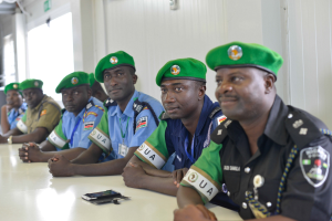 Eine Gruppe von Polizeibeamten sitzt an einem Tisch während einer Schulung, mit Mobiltelefonen und anderen Gegenständen auf dem Tisch, in einem Raum mit Fenstern und Deckenlampen.