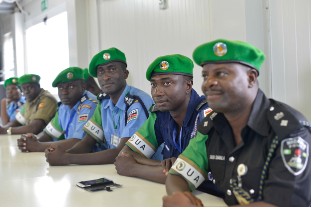 Eine Gruppe von Polizeibeamten sitzt an einem Tisch während einer Schulung, mit Mobiltelefonen und anderen Gegenständen auf dem Tisch, in einem Raum mit Fenstern und Deckenlampen.