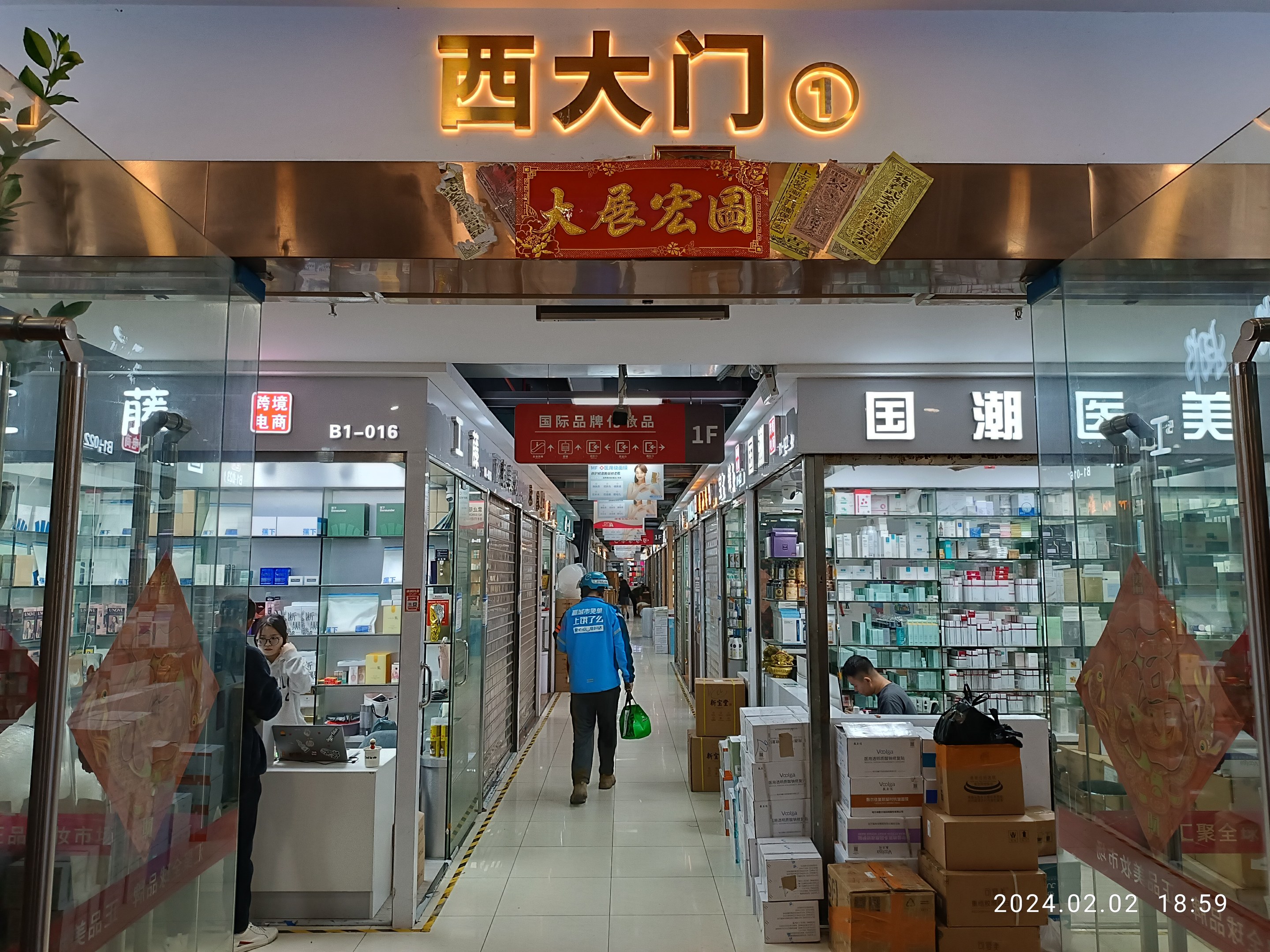 Innenansicht einer chinesischen Apotheke mit Glaswänden, Regalen voller Artikel, verstreuten Kartons auf dem Boden, einer Pflanze links und einer Namensschilder oben.