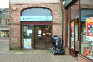 Eine Apothekenfiliale mit einem vor dem Gebäude geparkten Auto und einem Gebäude in der linken Ecke.