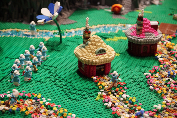 Ein Lego-Modell einer Kleinstadt mit zahlreichen Blumen, Spielzeugen, Häusern, Pflanzen und anderen Gegenständen vor einem leicht unscharfen Hintergrund.