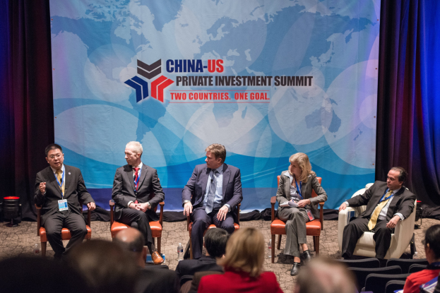 Eine Gruppe von Menschen, die auf Stühlen sitzen und auf einen Bildschirm schauen, auf dem Text und eine Karte zu sehen sind, mit Vorhängen im Hintergrund, während eines China-US-Privatinvestment-Gipfels.