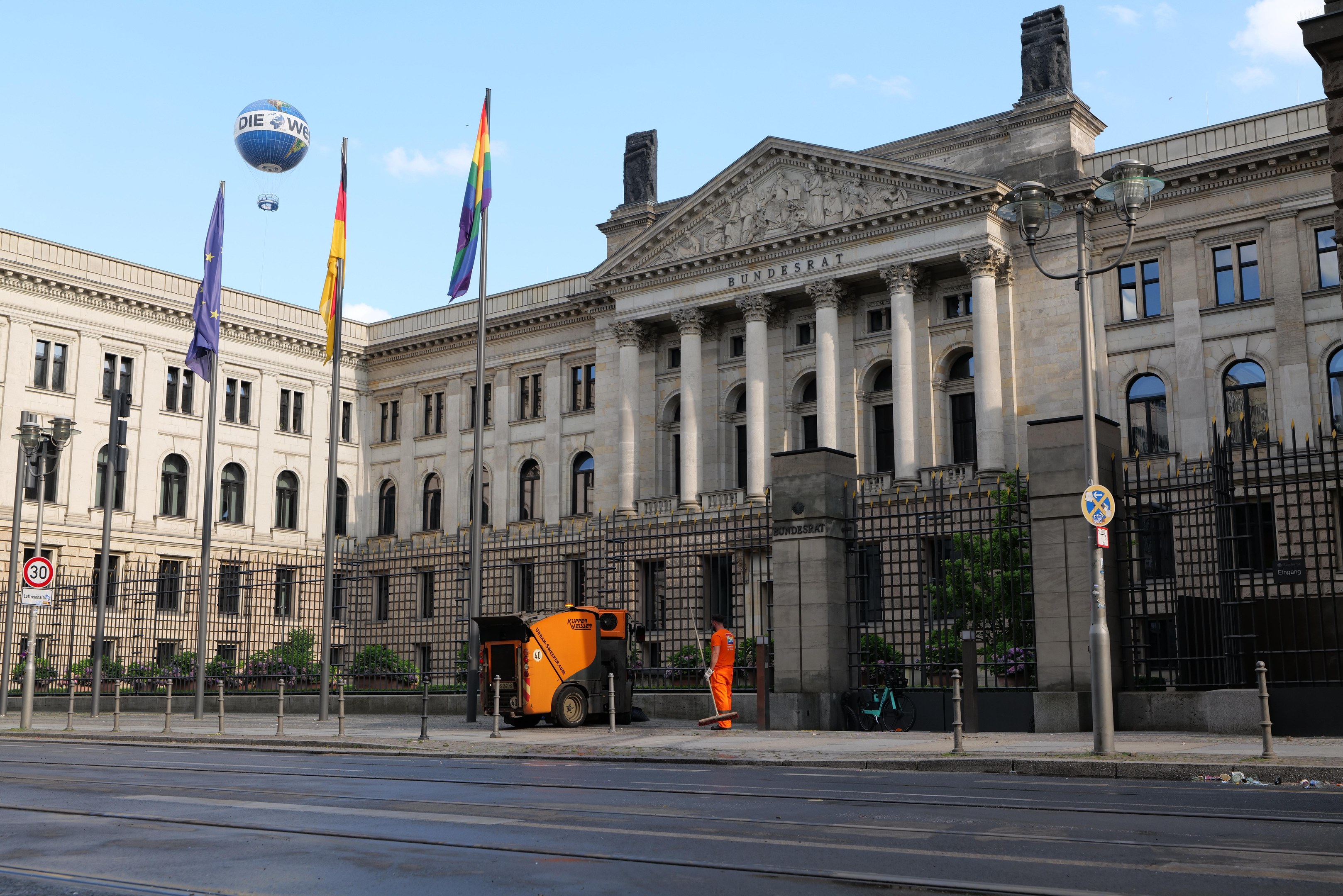 Großes modernes Gebäude mit zahlreichen Fenstern, als Bundestag in Berlin, Deutschland identifiziert, umgeben von Straßeninfrastruktur, Fahrzeugen, Fußgängern und Bäumen unter einem bewölkten Himmel.