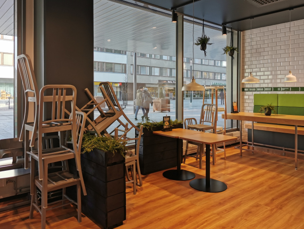 Ein Berliner Restaurant mit hölzernen Tischen und Stühlen vor einem großen Fenster, das eine Straßenszene mit Fußgängern, Gebäuden und städtischen Elementen zeigt.