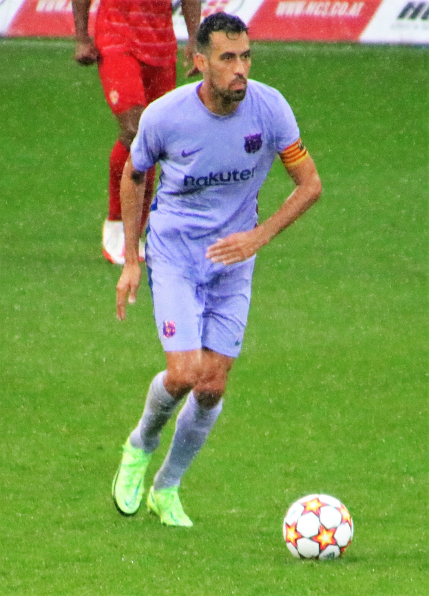Ein Fußballspieler in einem Sportoutfit und -schuhen ist im Einsatz auf dem Feld, mit einer Texttafel im Hintergrund.