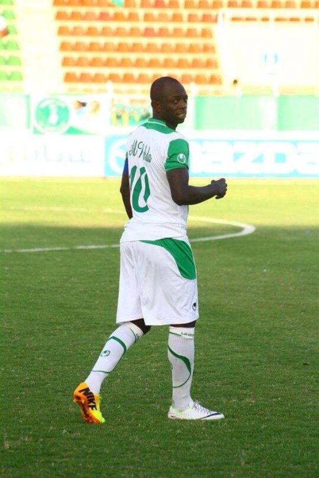 Ein Fußballspieler in einem grün-weißen Trikot feiert auf einem Feld umgeben von Werbetafeln und Stühlen, wahrscheinlich nach dem Gewinn der Afrikameisterschaft.