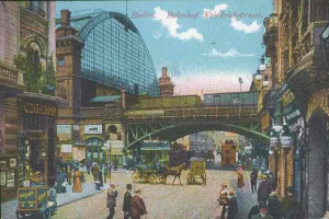 Alte Ansichtskarte, die eine belebte Berliner Straße mit Fußgängern, Pferdewagen, Gebäuden, Laternen, einer Brücke und einem bewölkten Himmel zeigt, mit Text oben.