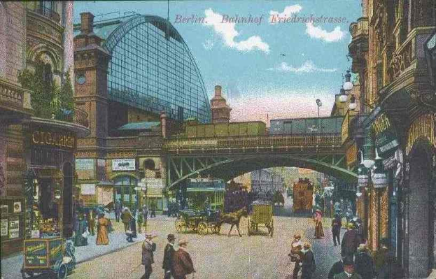 Alte Ansichtskarte, die eine belebte Berliner Straße mit Fußgängern, Pferdewagen, Gebäuden, Laternen, einer Brücke und einem bewölkten Himmel zeigt, mit Text oben.