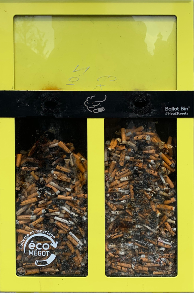 Gelber Müllsack voller Zigarettenstummel auf einem Gehweg, beschriftet für Zigarettenabfall.