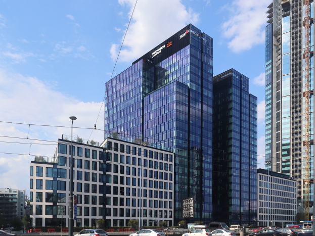 Hauptsitz der Deutschen Bank in Frankfurt, Deutschland, ein großes Gebäude mit vielen Fenstern, umgeben von städtischer Infrastruktur und Grünflächen unter einem bewölkten Himmel.