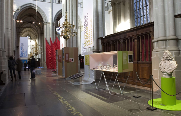 Ein großer Museumsraum mit verschiedenen Artefakten, darunter eine Statue auf einem Sockel, Absperrbahnen, Textbanner, Säulen und Kronleuchter, sowie einige Besucher.