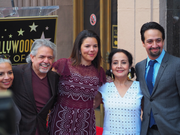 Gruppe von Menschen, die auf dem roten Teppich bei der Zeremonie des Hollywood Walk of Fame posen, mit einer Tafel, einem Glaspodest und einer Wand im Hintergrund.