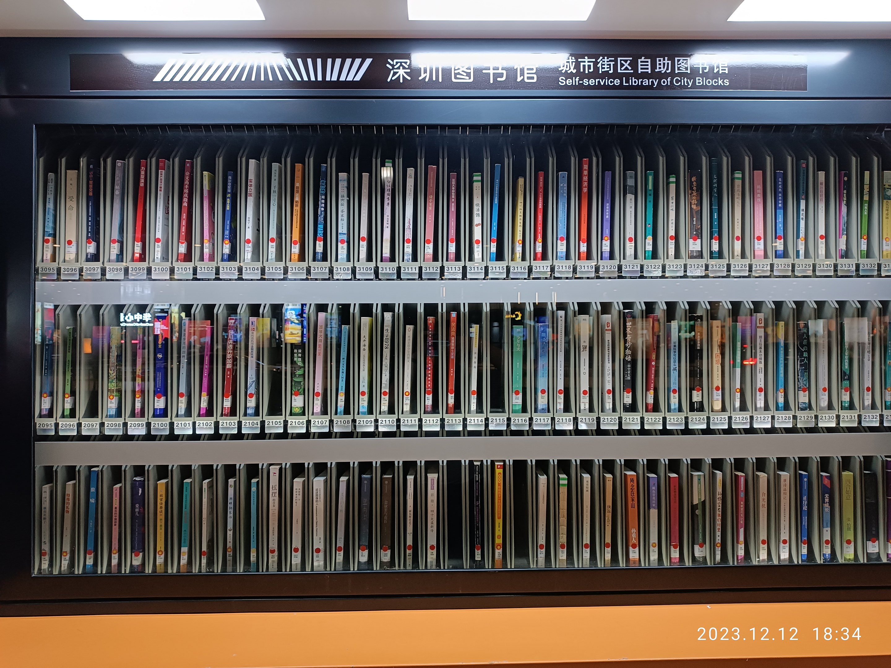 Eine gut beleuchtete Bibliothek mit hohen Bücherregalen voller Bücher, mit einem Textschild und einem Wasserzeichen unten, das an eine Selbstbedienungsbibliothek von Stadtblöcken erinnert.