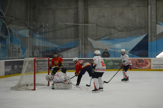 Eine Gruppe von Menschen, die Eisockey auf einer Indoor-Eisfläche spielt, mit Helmen und Hockey-Schlägern ausgestattet, mit einem Torpfosten links und Bannern im Hintergrund.
